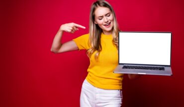 Portrait of young woman holding, working on laptop pc computer isolated on red background.