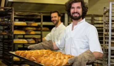 smiling-baker-carrying-tray-freshly-baked-french-baguette_1170-2290